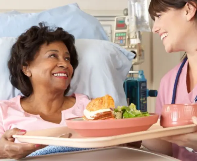 Caregiver feeding a dependent patient sitting upright in a hospital bed