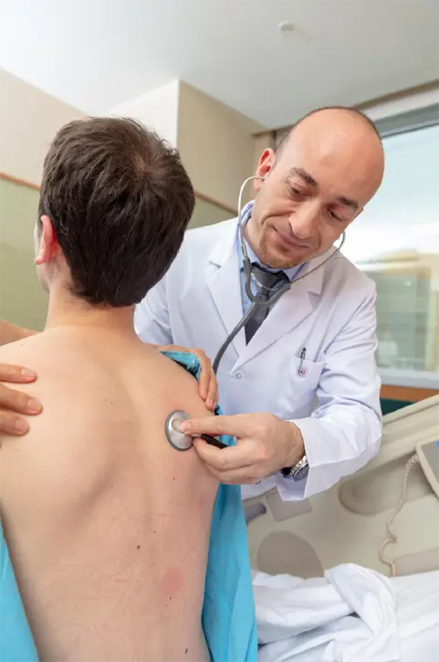 Doctor listening to a patient's lungs with a stethoscope in a hospital examination room